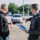 A driving instructor explain rules to a learner driving at a test centre with a car far at the distant background